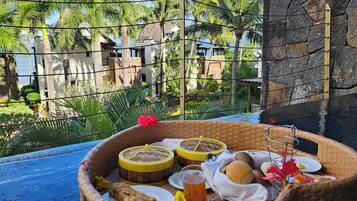 Una cesta de mimbre llena de comida y bebidas en una zona junto a la piscina, con vista a un resort y palmeras.