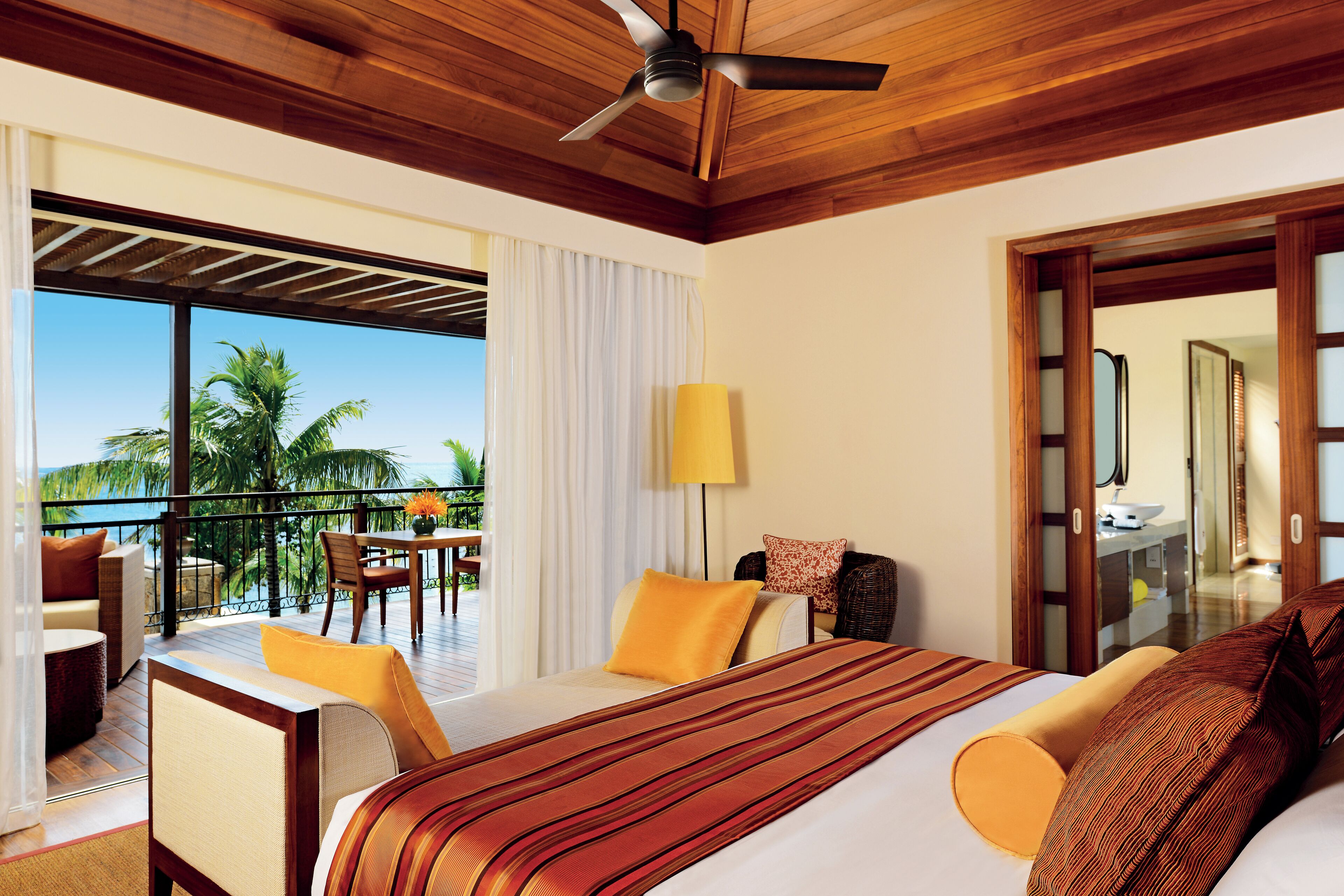 A hotel room with a large bed, a balcony with a table and chairs, and a view of palm trees.
