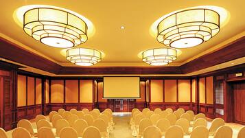 Un salón de conferencias con filas de sillas, una pantalla grande y tres candelabros.