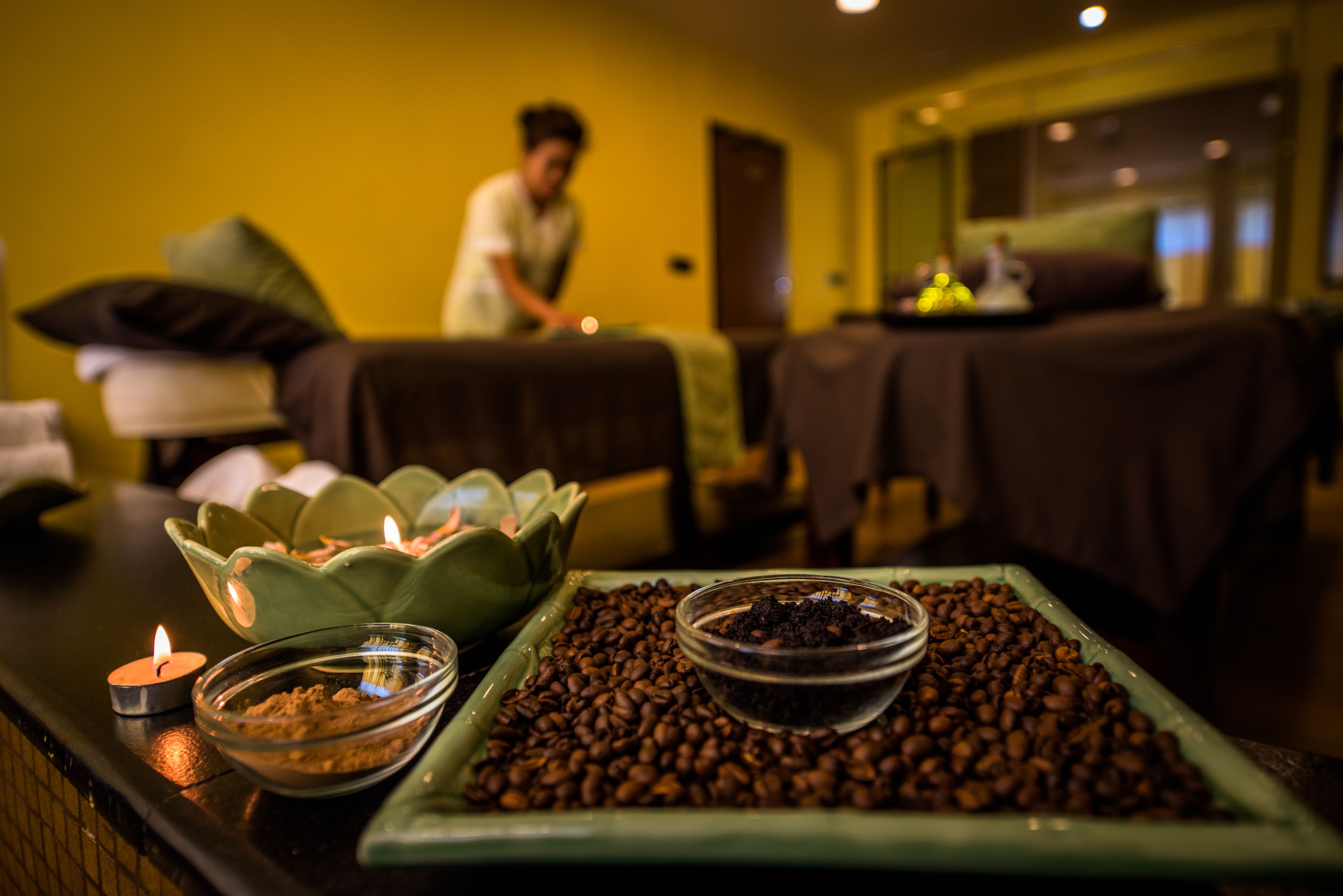 Um quarto com mesa de massagem, um recipiente com grãos de café e uma vela sobre uma mesa.