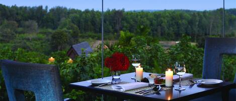 Mesa preparada para dos con velas, un jarrón de flores rojas y vistas a un paisaje boscoso.