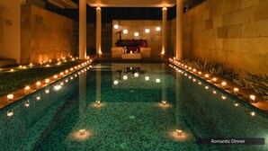 A poolside area with a seating arrangement under a covered structure, surrounded by candles and plants. - The Serai Chikmagalur (Chikkamagaluru)