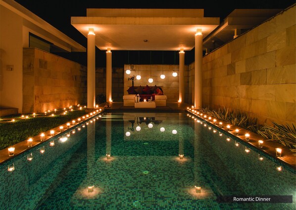 Zona de piscina con disposición de asientos bajo una estructura cubierta, rodeada de velas y plantas.