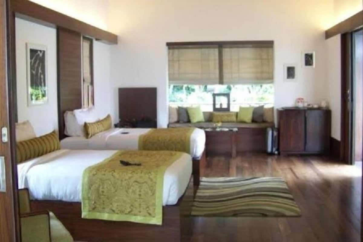 A hotel room with two beds, a sofa, a desk, and a window with blinds.