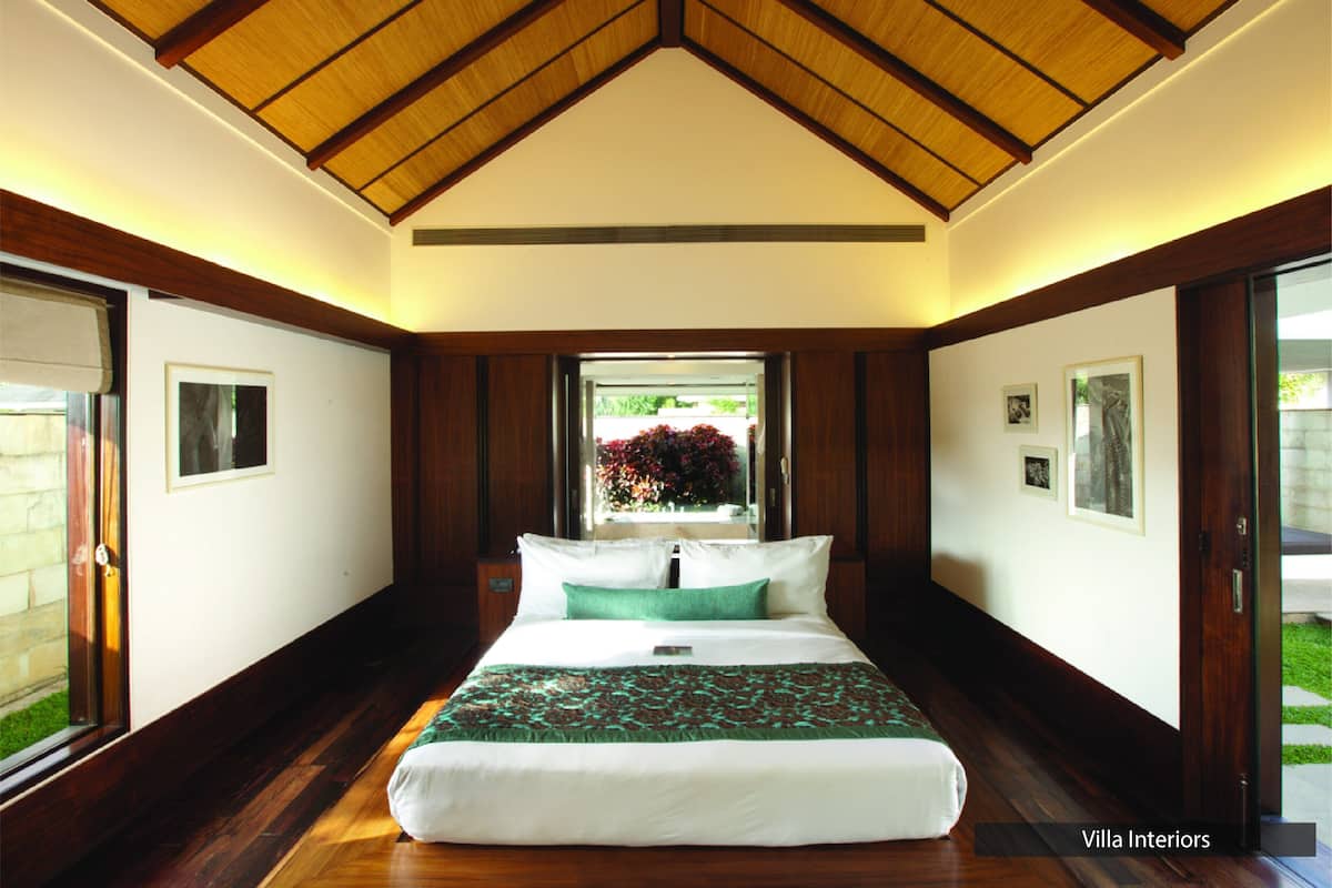 A bedroom with a large bed, wooden ceiling, and a view of a garden through a window.