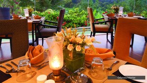 A dining table set with a vase of flowers, a lit candle, and various tableware. - The Serai Chikmagalur (Chikkamagaluru)