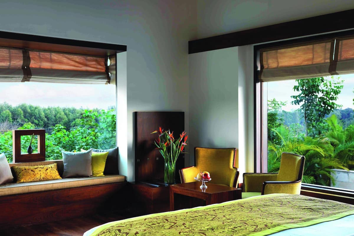 A bedroom with a bed, a bedside table with a vase, a chair, and a sofa with cushions.
