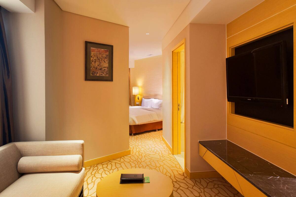 A hotel room with a sofa, a bed, a TV, and a small table with a remote control.
