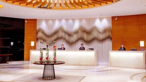 A modern hotel lobby with a reception desk, a round table with a vase of flowers, and a unique ceiling design. - Radisson Hotel Tianjin Aqua City (Tianjin)