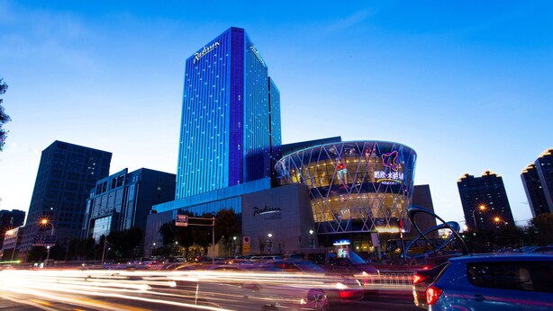 A modern hotel with a prominent tower and a curved building with neon signage. - Radisson Hotel Tianjin Aqua City (Tianjin)