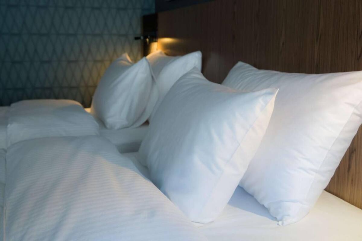 A bed with white bedding and pillows, a wooden headboard, and a patterned wall in the background.