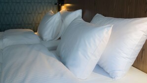A neatly made bed with white linens and pillows, a wooden headboard, and a patterned wall in the background. - Radisson Hotel Tianjin Aqua City (Tianjin)