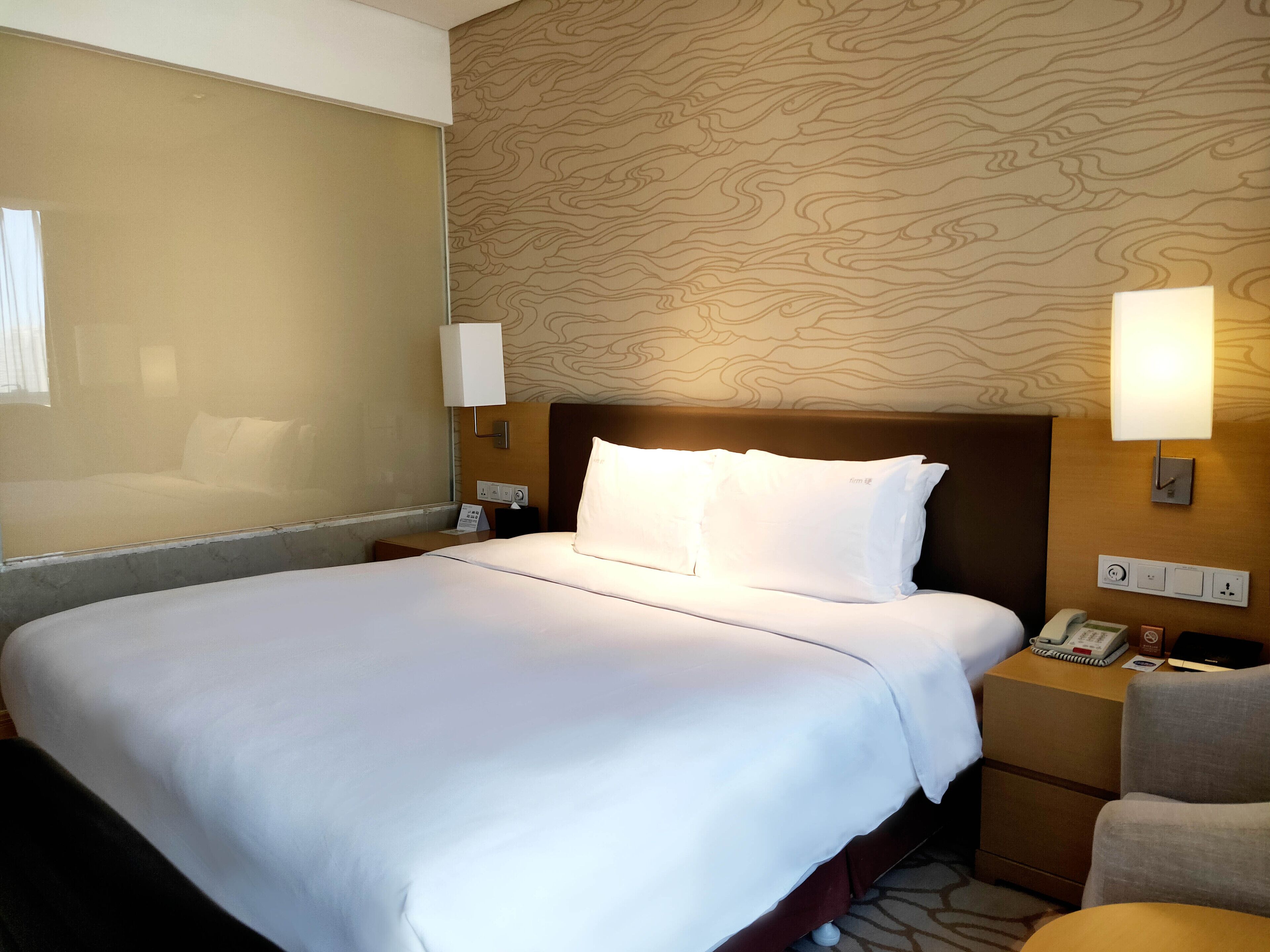Habitación de hotel con una cama grande, dos lámparas de noche, un mesita de noche con un teléfono y una silla.