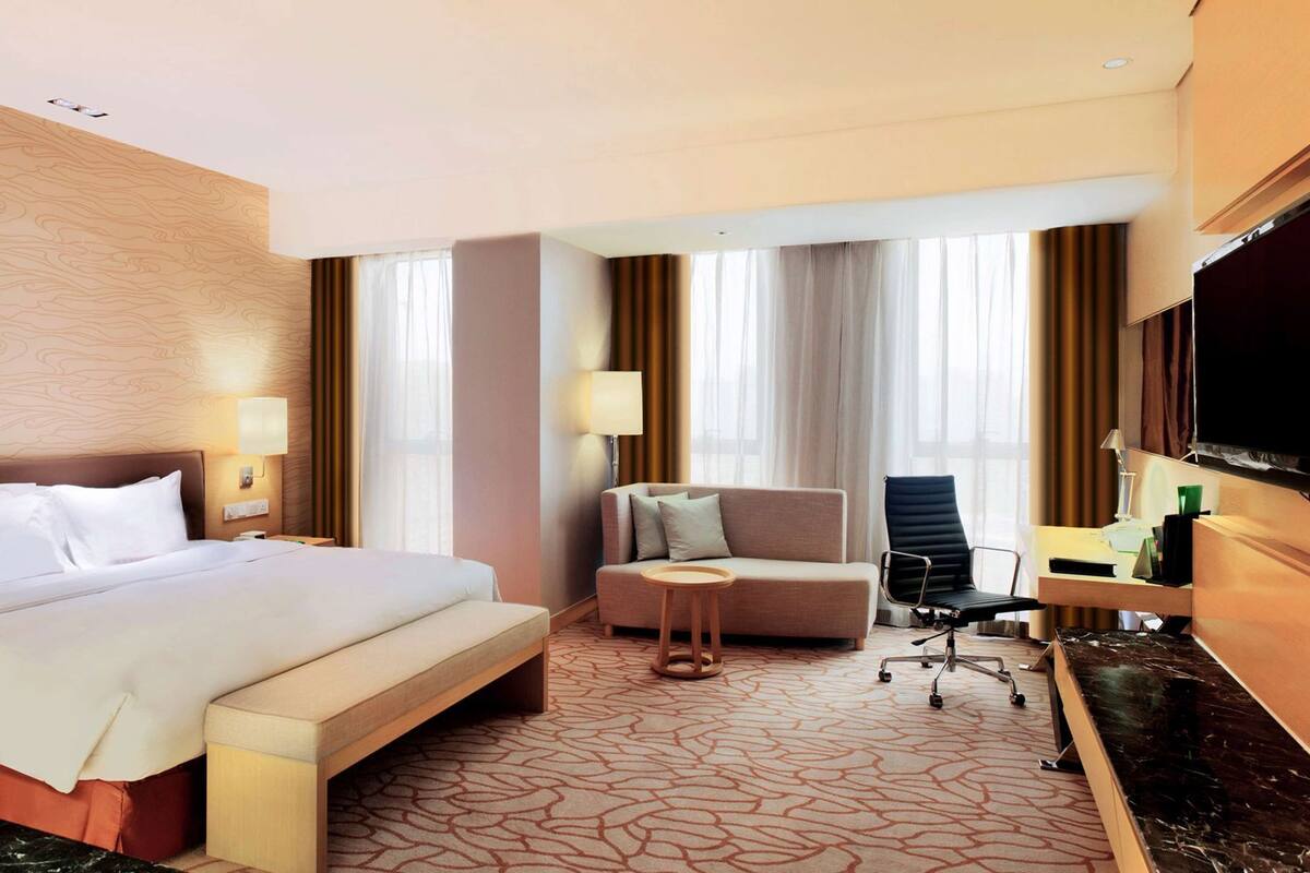 A hotel room with a bed, a sofa, a desk, a chair, and a TV.