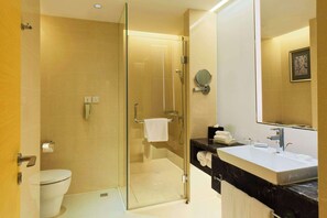 A modern bathroom with a glass-enclosed shower, a white toilet, and a black marble sink with a large mirror. - Radisson Hotel Tianjin Aqua City (Tianjin)