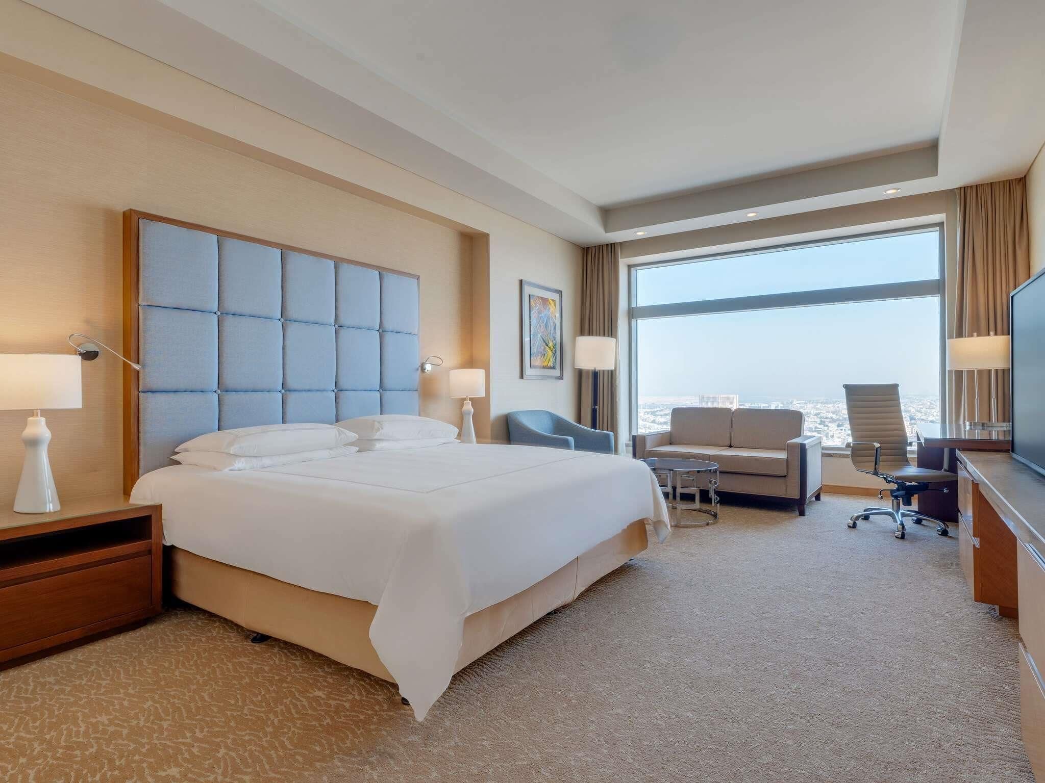 A hotel room with a large bed, a desk, a chair, and a TV.
