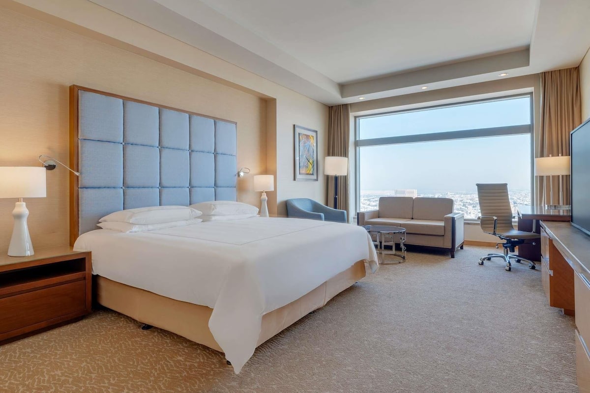 A hotel room with a large bed, a desk, a chair, and a TV.
