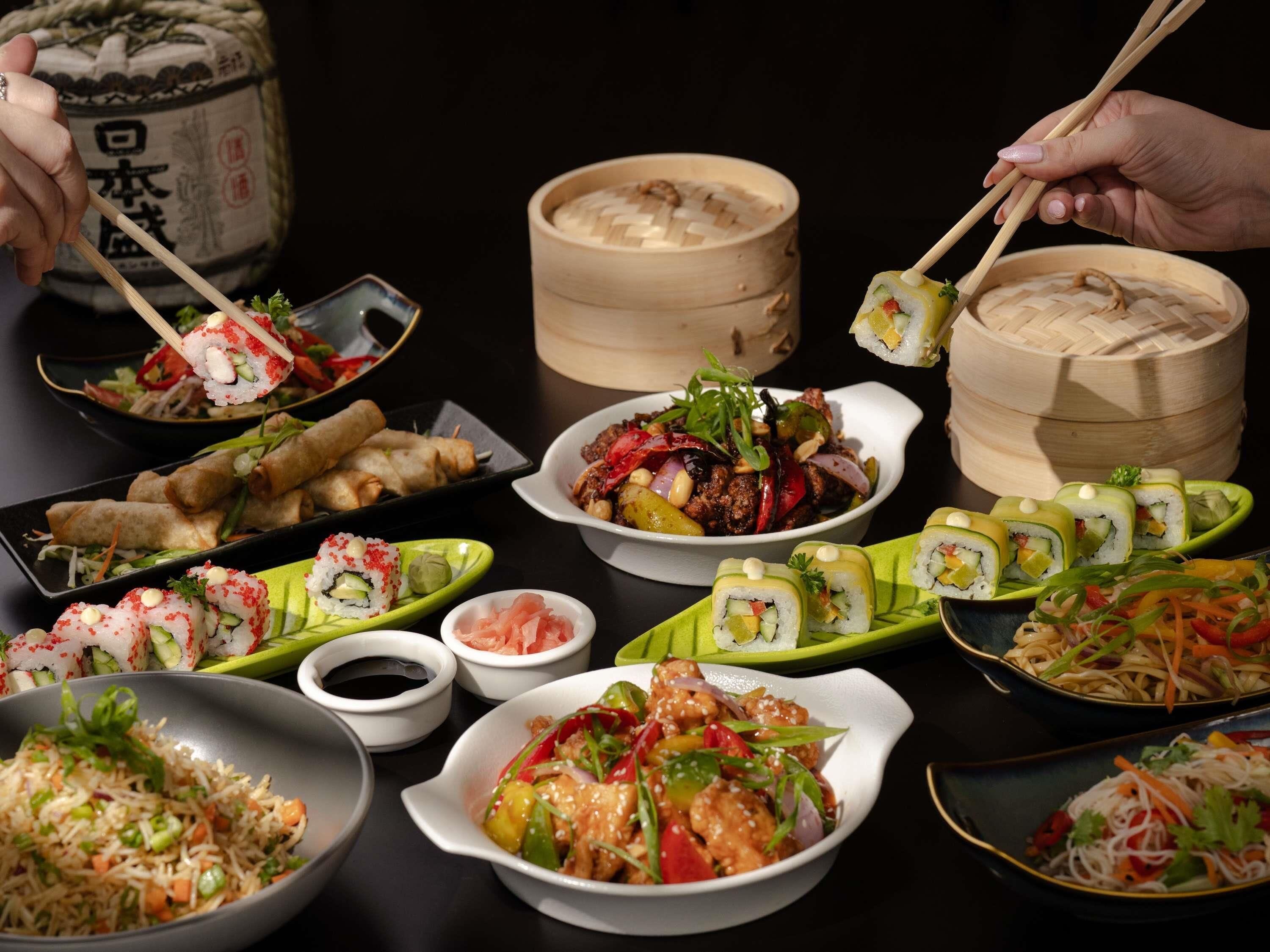 Verschiedene asiatische Gerichte, darunter Sushi, Frühlingsrollen und eine Schüssel gebratenes Gemüse.