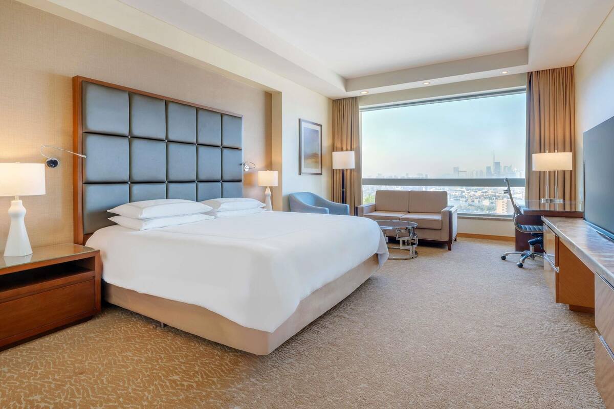A hotel room with a large bed, a desk, a chair, a sofa, and a TV.