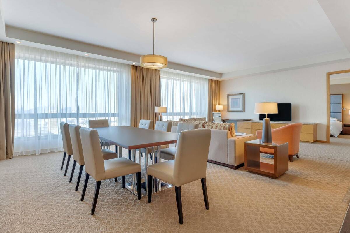A hotel room with a dining area, a sofa, a TV, and a bed.