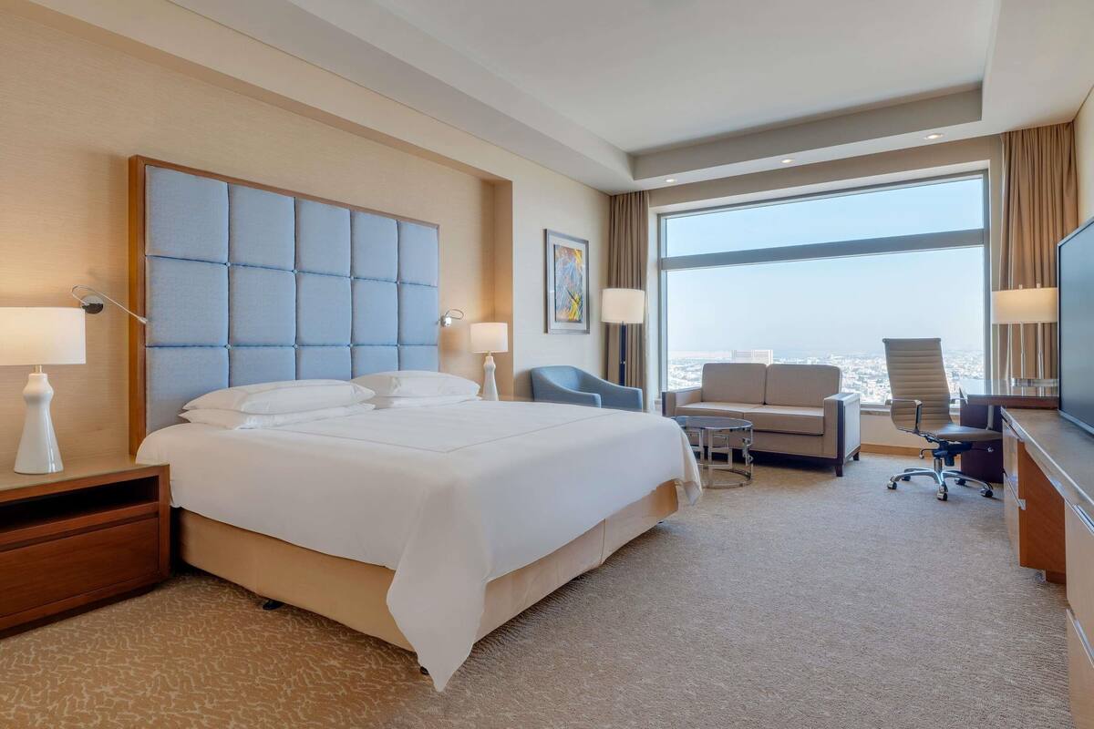 A hotel room with a large bed, a desk, a chair, and a television.