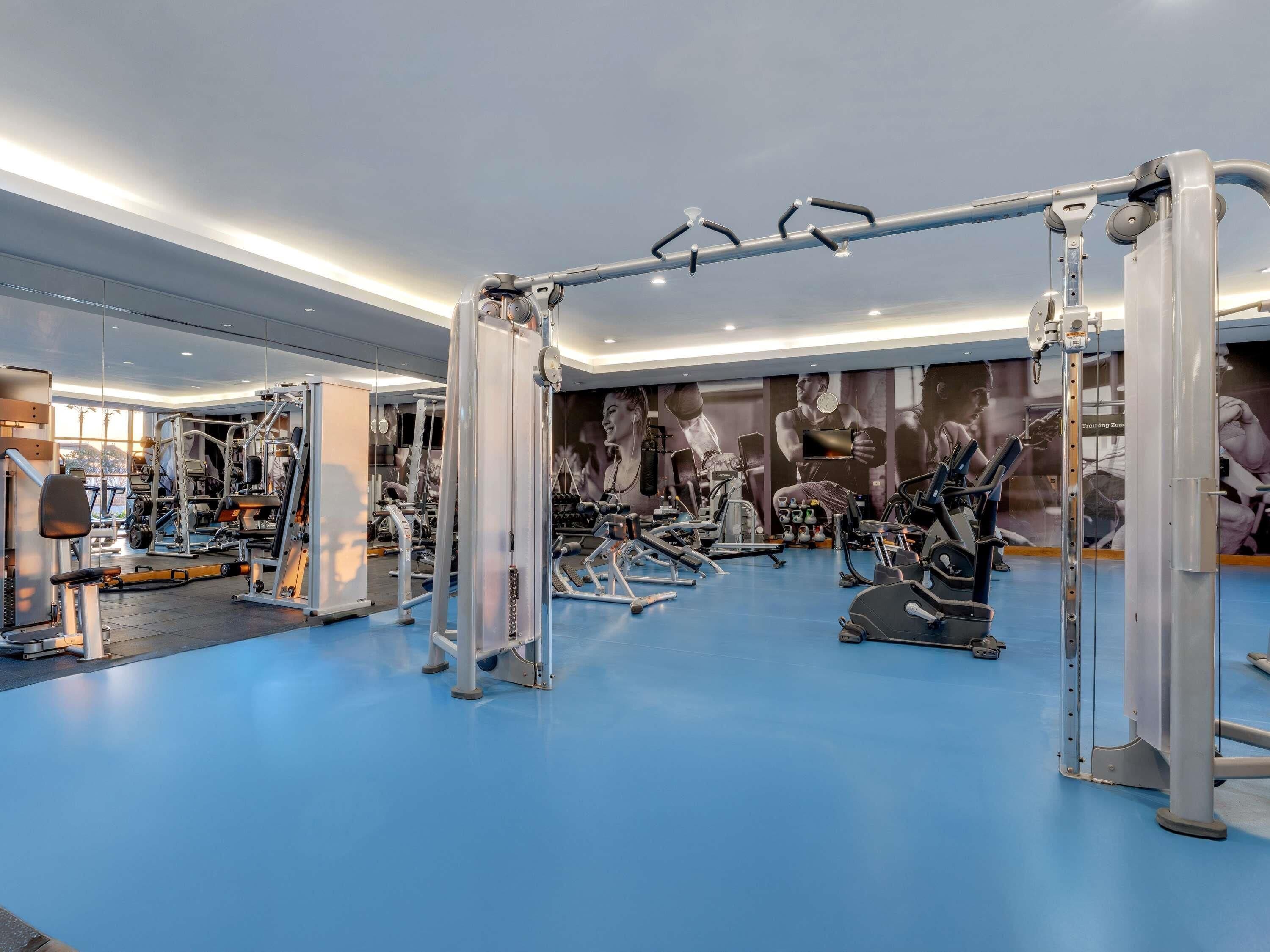 A modern gym with various exercise machines, a pull-up bar, and a blue floor.