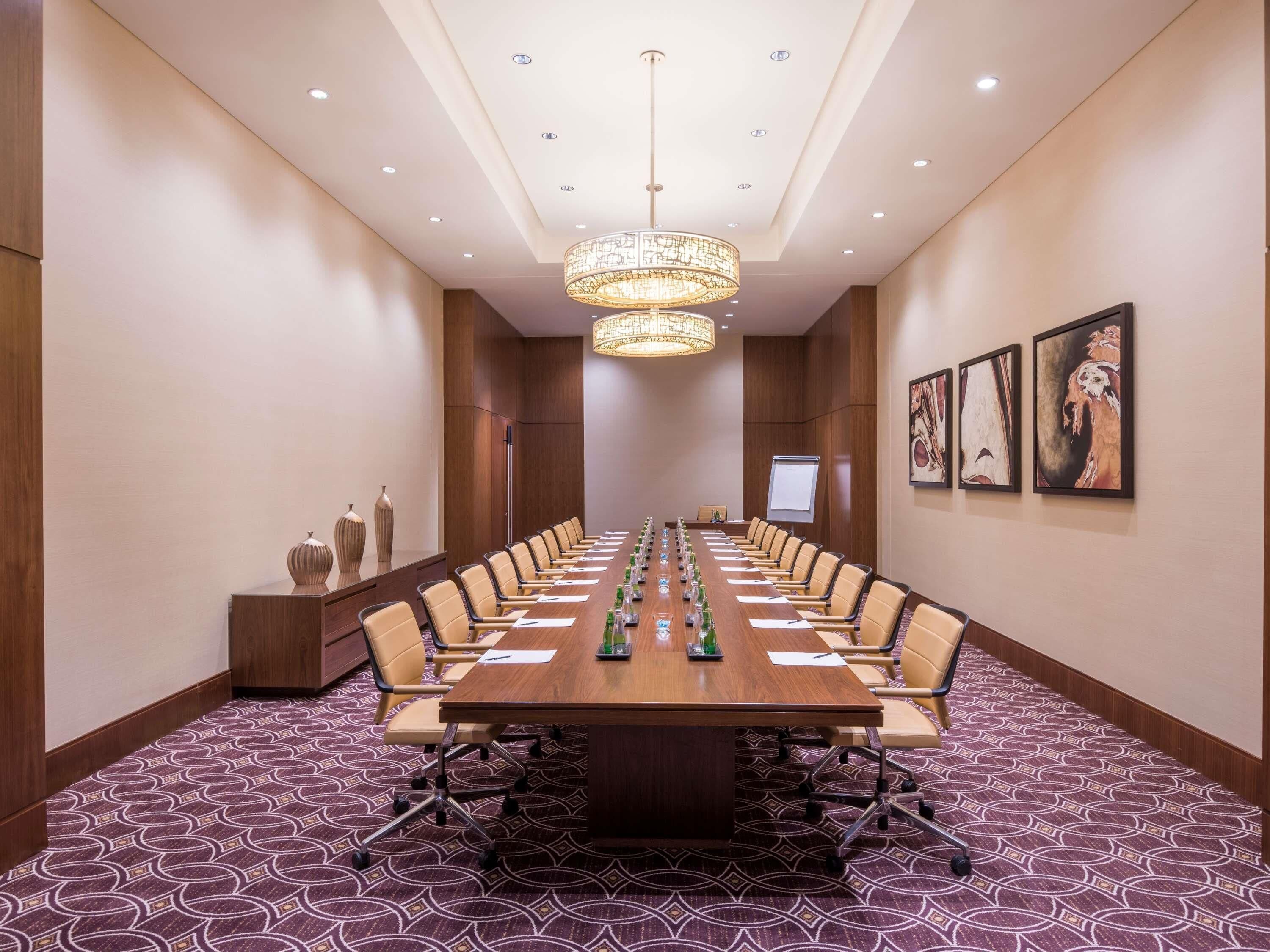 A conference room with a long table, chairs, a projector screen, and a patterned carpet.