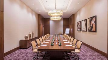 A conference room with a long table, chairs, a projector screen, and a patterned carpet.