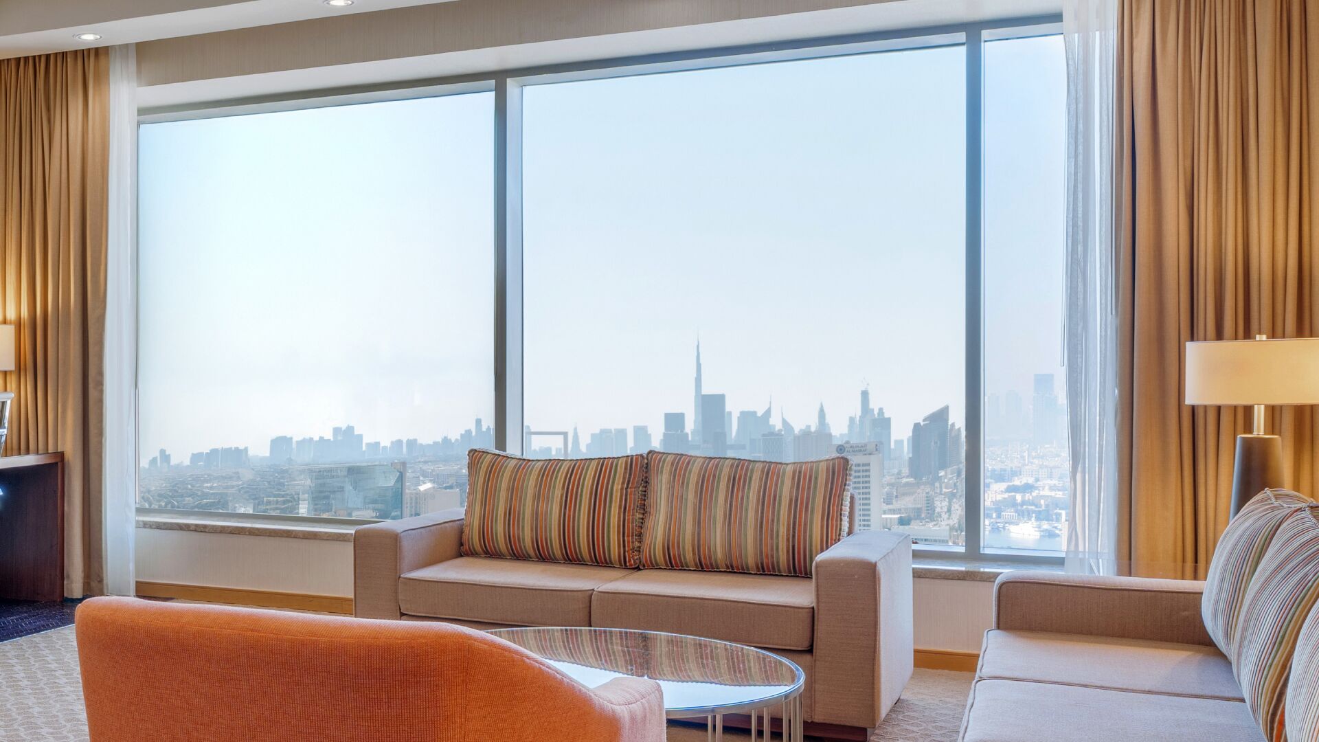 A hotel room with a large window, a sofa, a round coffee table, and a lamp.