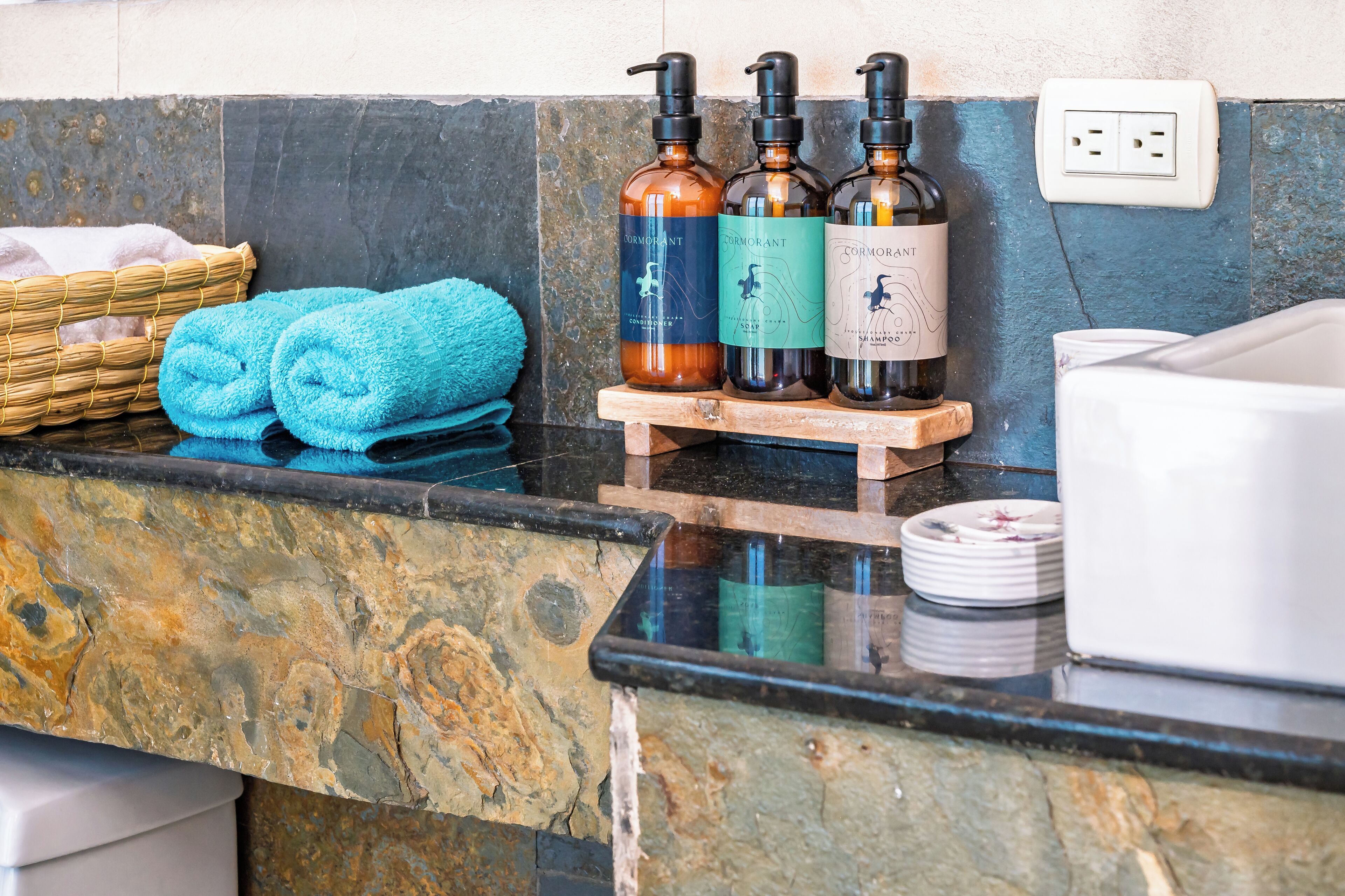 A bathroom counter with toiletries, towels, and a small wooden stand.