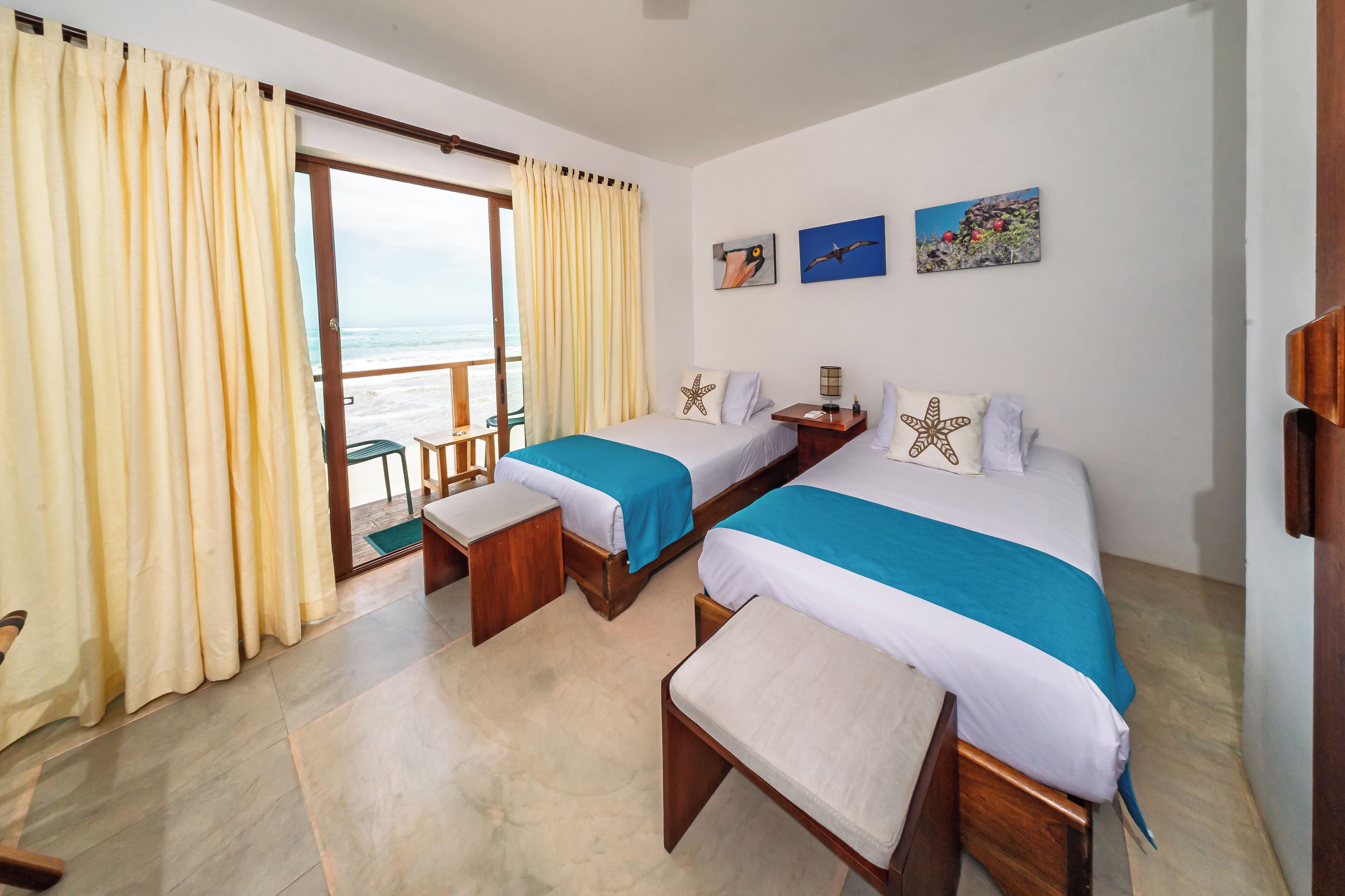 Een hotelkamer met twee bedden, uitzicht op zee en twee aan de muur bevestigde foto's.
