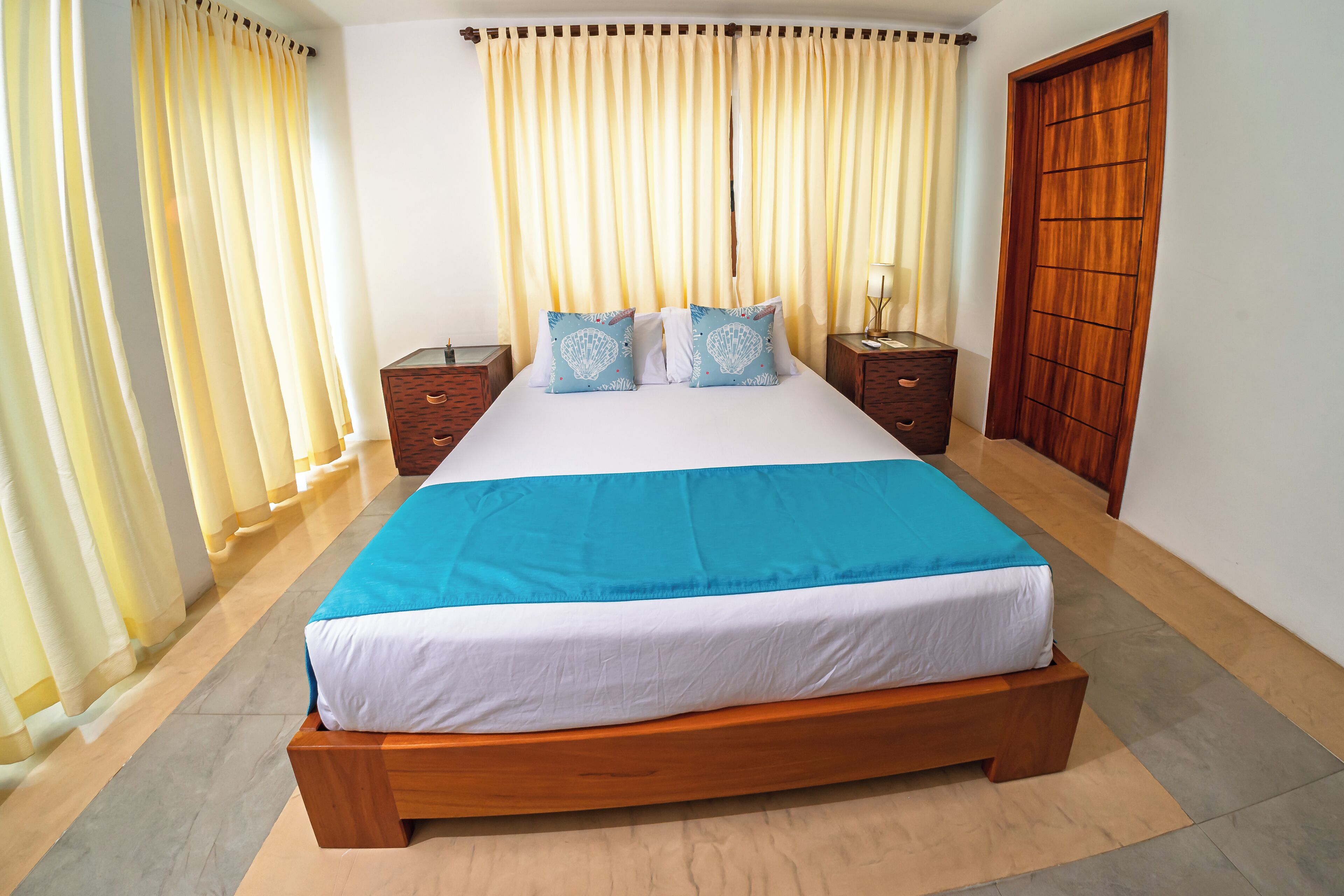 A large bed with a blue and white bedspread, two matching pillows, wooden headboards, and a wooden wardrobe.