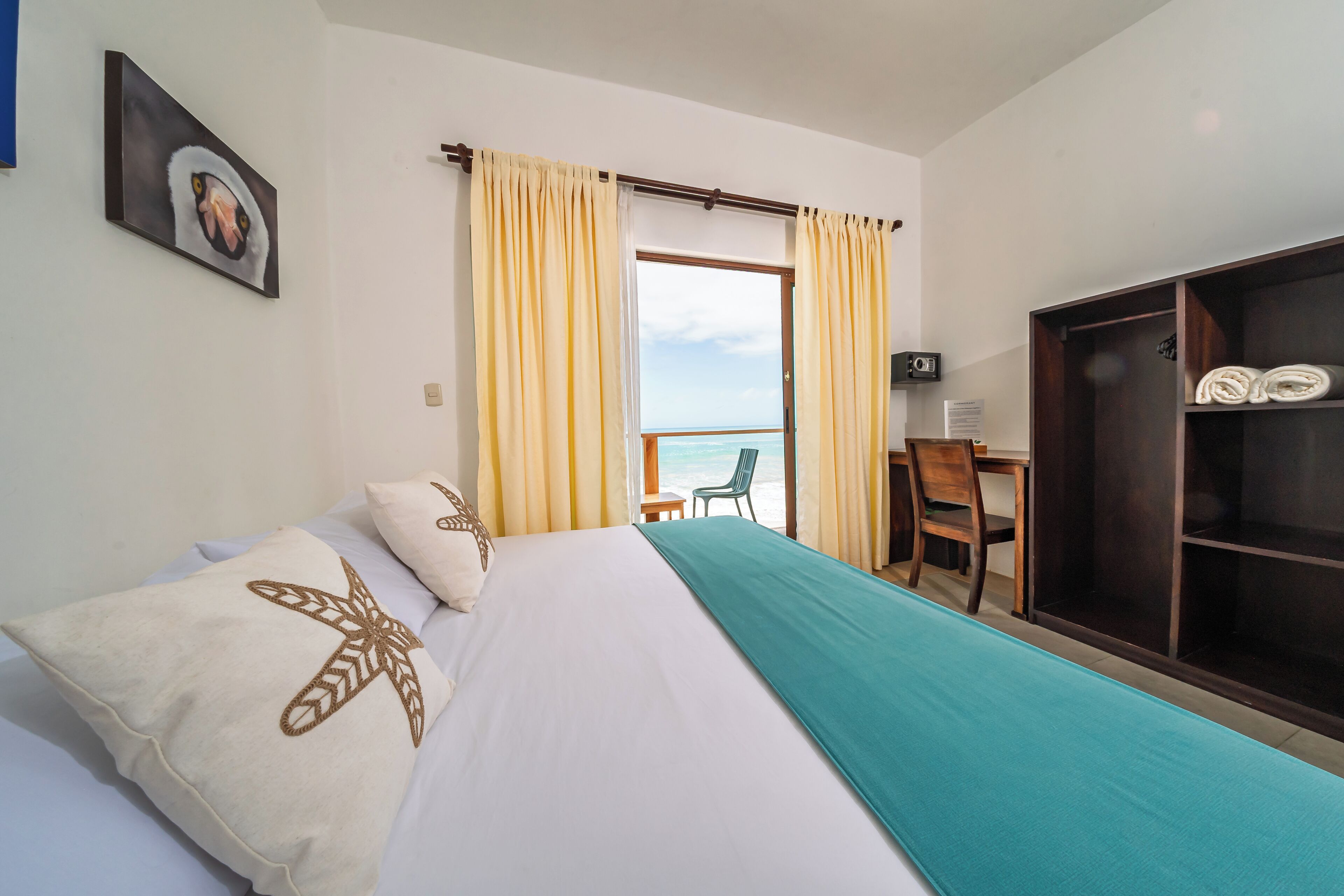 A hotel room with a bed, a desk, a chair, a wardrobe, and a view of the sea.