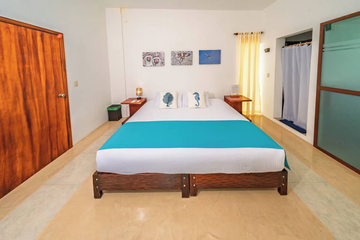 A bedroom with a wooden bed, a wooden wardrobe, a nightstand with a lamp, and a wall with three framed pictures.