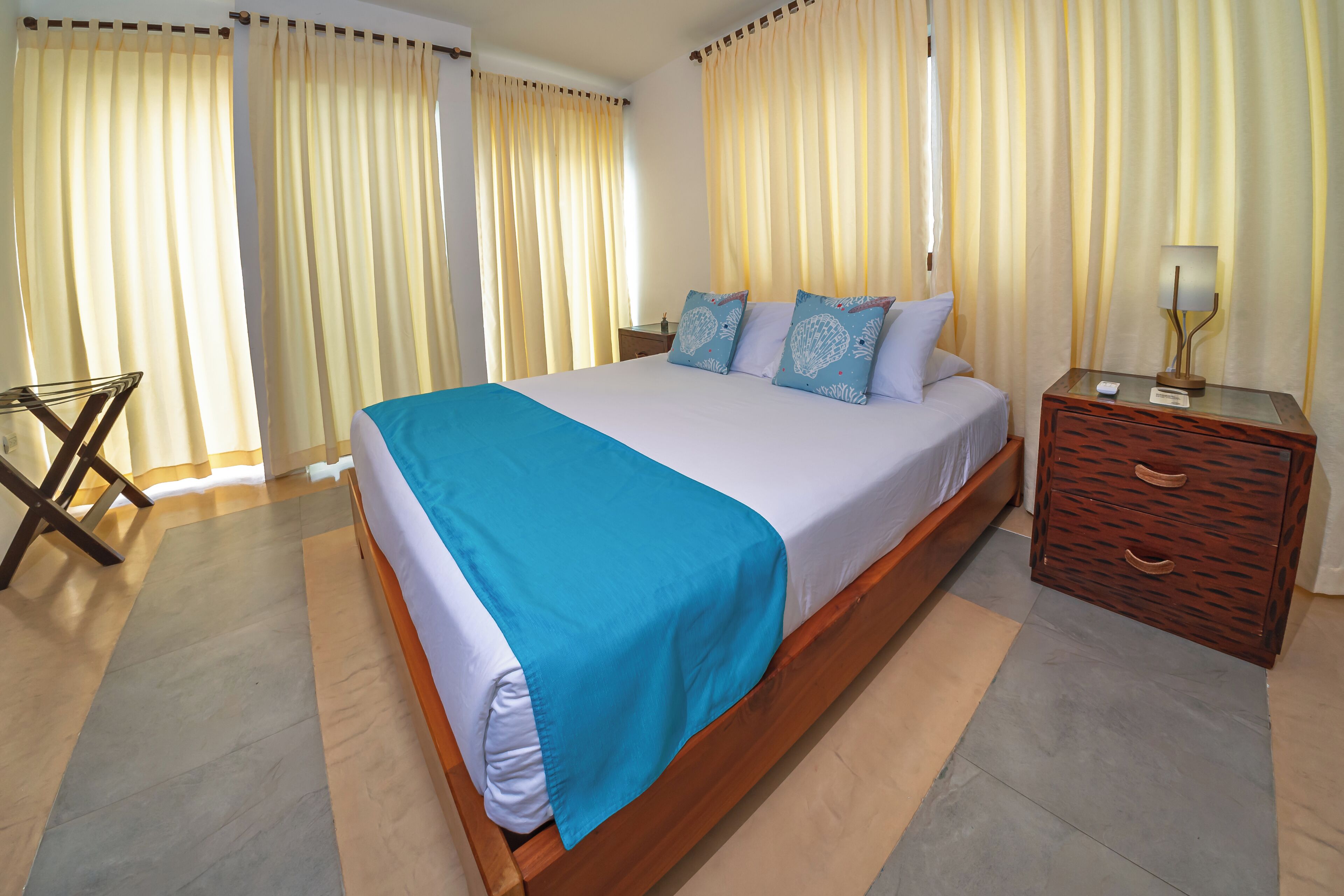 A hotel room with a large bed, a wooden nightstand, a lamp, and curtains.