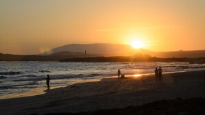 Escena de playa al atardecer con gente de pie sobre la arena.
