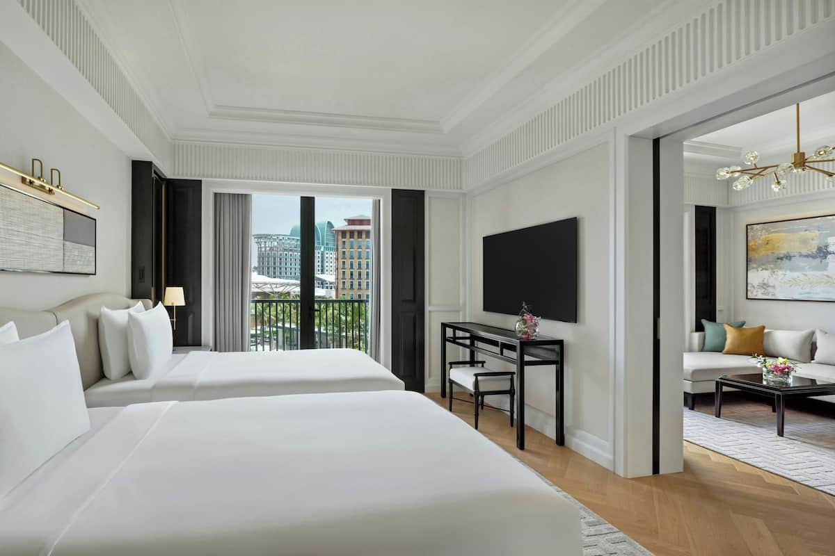 Een hotelkamer met twee bedden, een bureau, een televisie en een balkon met uitzicht over de stad.