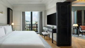 A hotel room with a large bed, a desk, a TV, and a balcony with a view of the city.