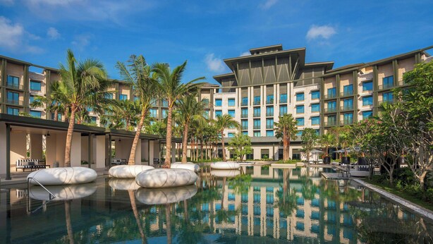 Un hotel con una piscina grande, palmeras y arquitectura moderna.