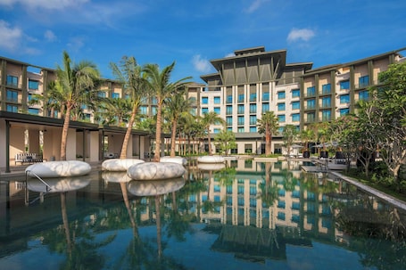 A hotel with a large pool, palm trees, and modern architecture.