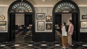 Un vestíbulo con suelo estampado en blanco y negro, obras de arte enmarcadas en las paredes y un candelabro.