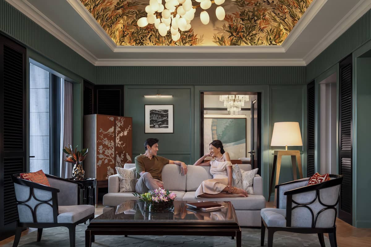 Een ruime woonkamer met een zithoek, een salontafel en een decoratief plafond.