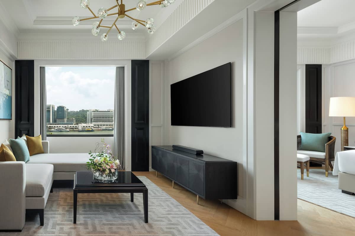 Een moderne hotelkamer met een bank, een flatscreen televisie, een bijzettafeltje met bloemen en uitzicht op de stad.