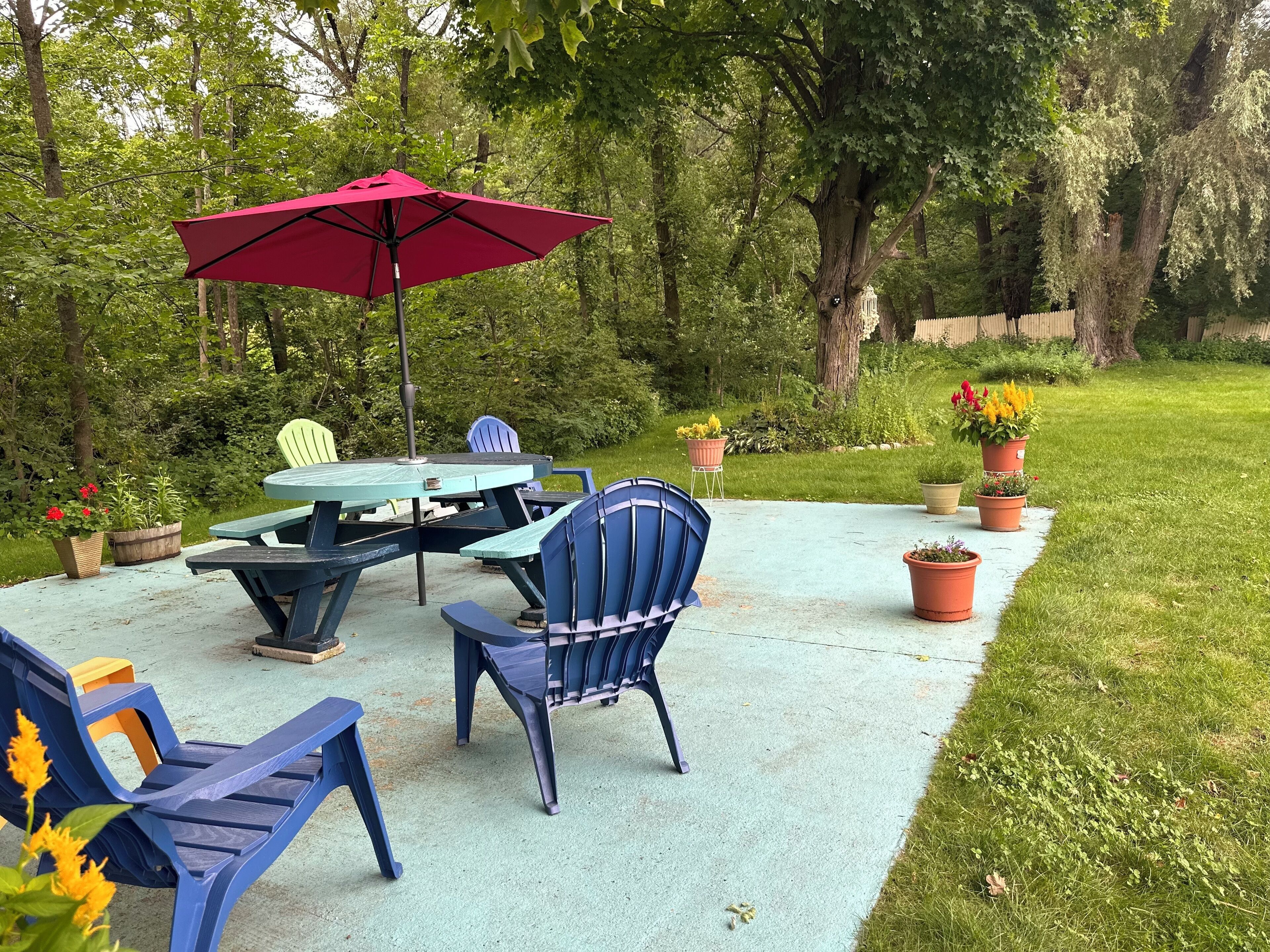 Eine Terrasse im Freien mit Tisch und Stühlen, umgeben von Topfpflanzen und einem roten Sonnenschirm.