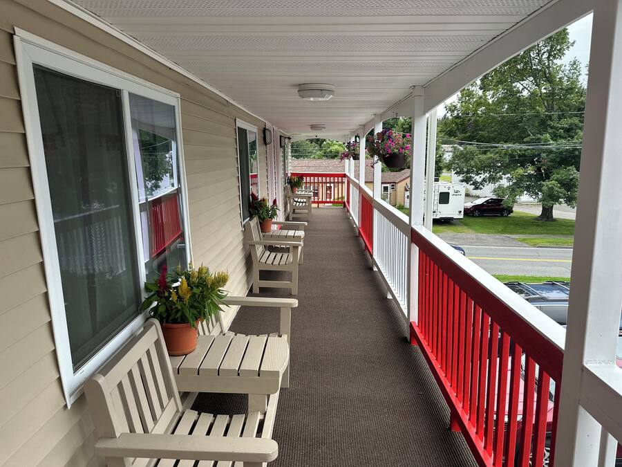 A covered porch with beige siding, white railings, and a row of wooden benches.