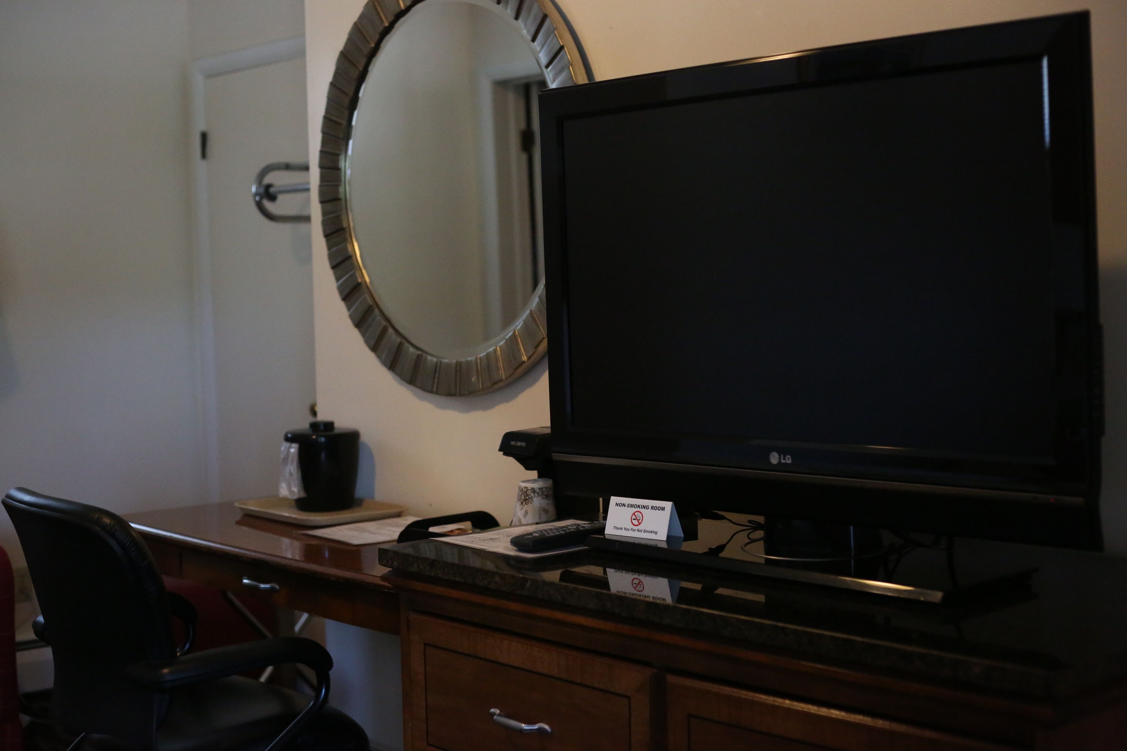 Une chambre d’hôtel équipée d’un téléviseur à écran plat, d’un bureau en bois, d’un fauteuil de bureau noir, d’une machine à café et d’une pancarte indiquant qu’il s’agit d’une chambre non-fumeur.