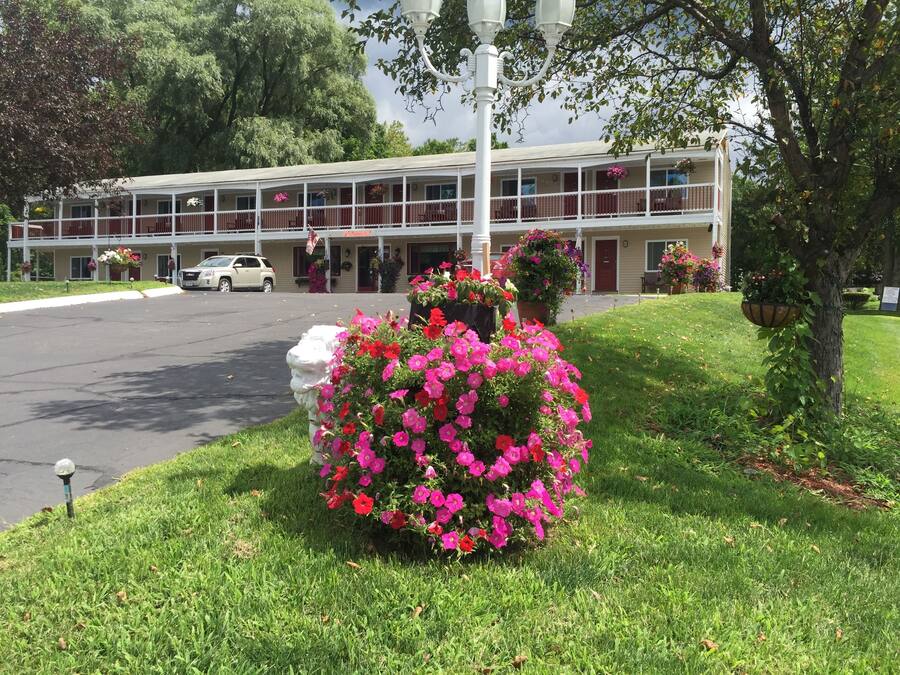 A motel with a two-story structure, a covered parking area, and a well-maintained lawn with a flower bed.