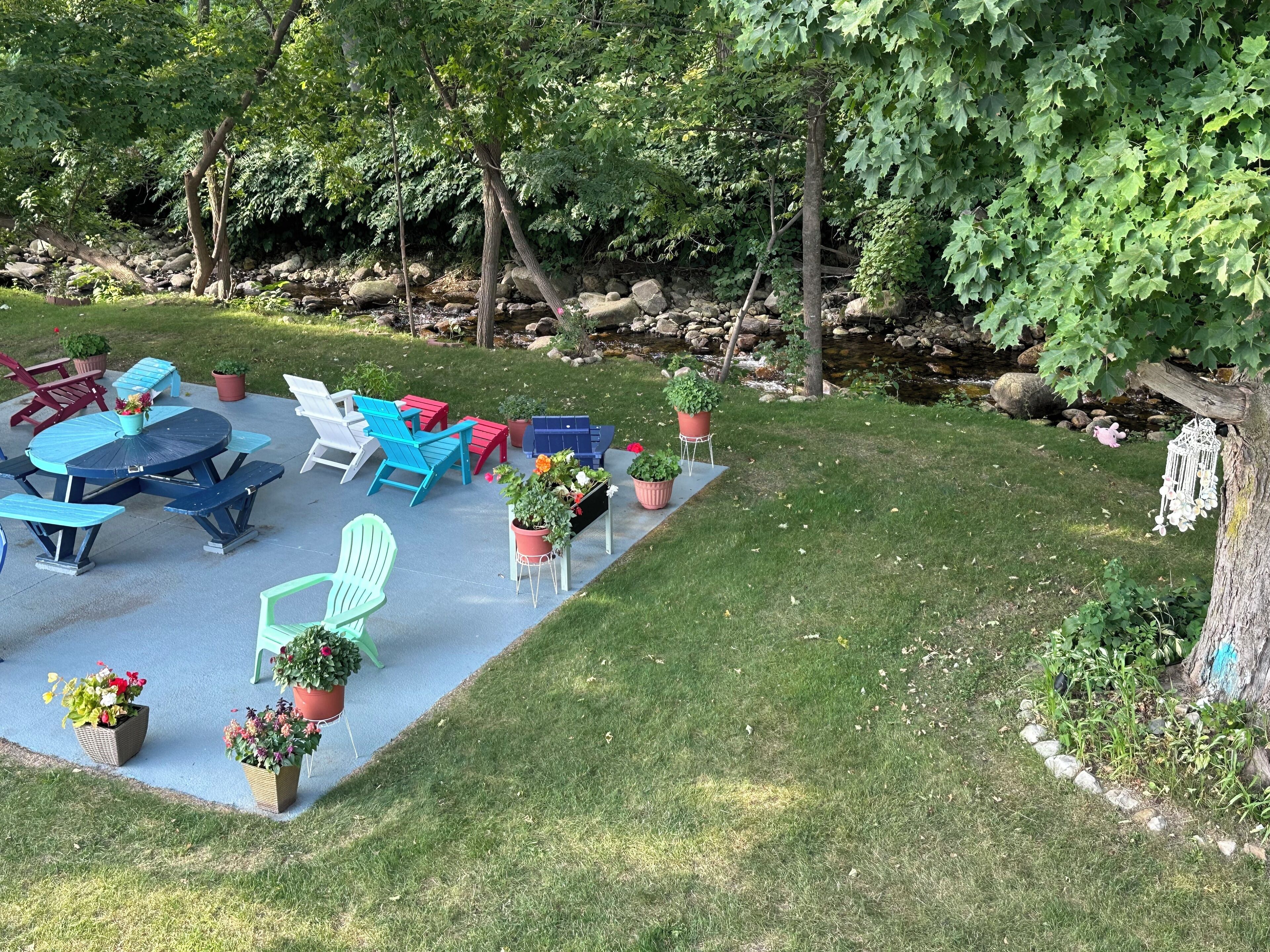 An outdoor patio with a table and chairs, surrounded by potted plants and a small stream.