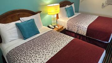 Habitación de hotel con dos camas, cada una con una colcha estampada, una lámpara de noche y un teléfono en la mesita.