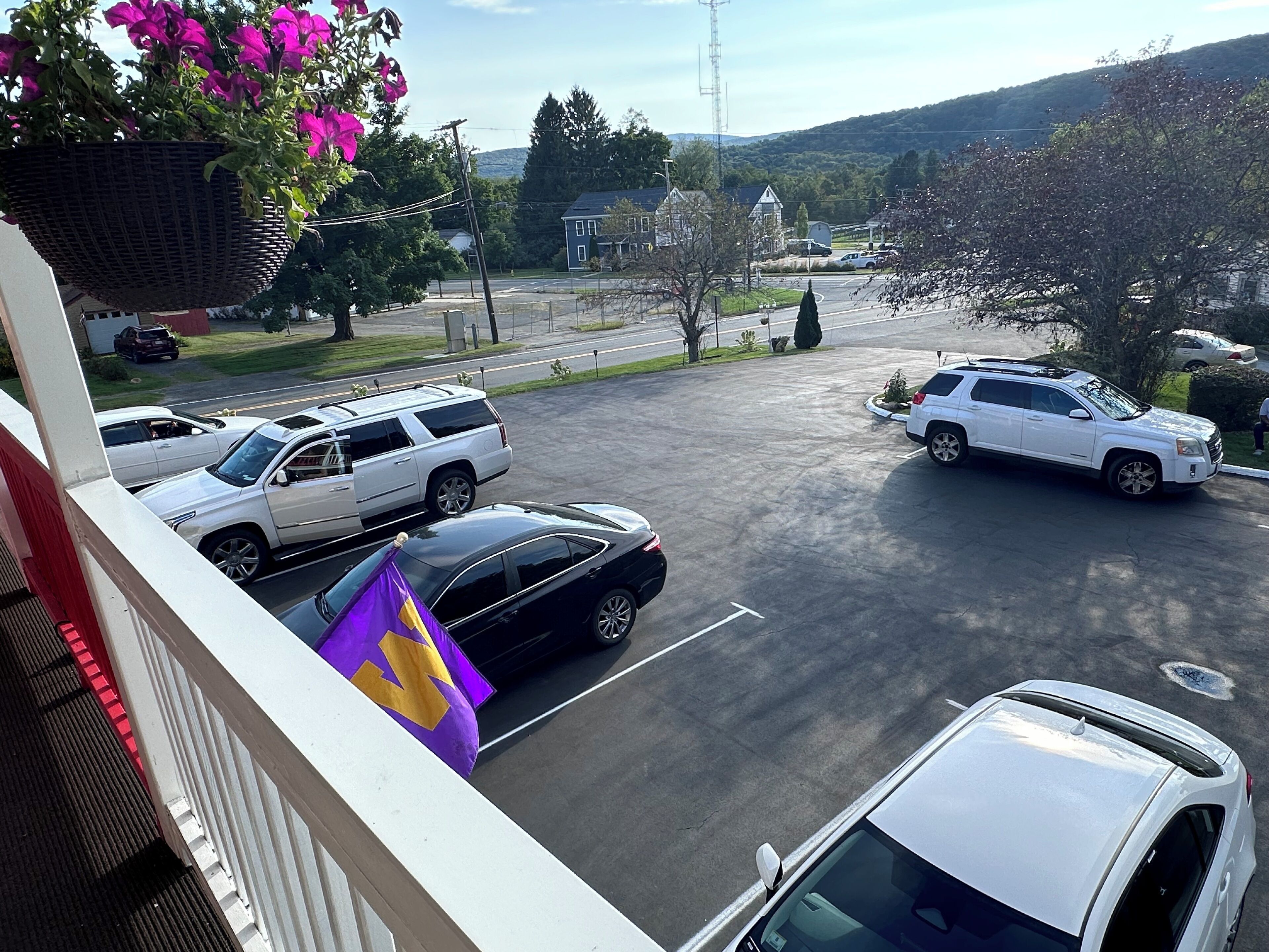 Un estacionamiento con varios coches, un edificio blanco y una colina al fondo.